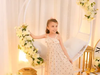 Menina em vestido floral elegante ao lado do balanço ninho decorado com flores brancas e luzes no cenário de Ano Novo