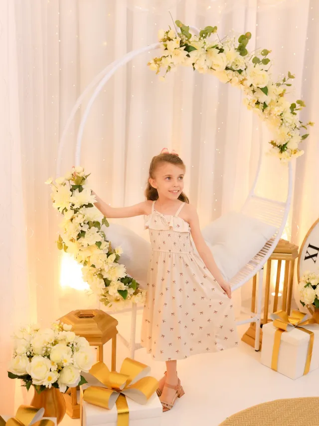 Menina em vestido floral elegante ao lado do balanço ninho decorado com flores brancas e luzes no cenário de Ano Novo