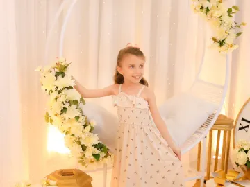Menina em vestido floral elegante ao lado do balanço ninho decorado com flores brancas e luzes no cenário de Ano Novo