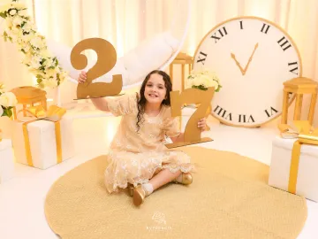 Cenário de Ano Novo no Estúdio Evydência: menina em vestido champanhe com números dourados e grande relógio às 11:55