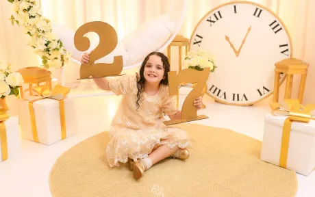 Cenário de Ano Novo no Estúdio Evydência: menina em vestido champanhe com números dourados e grande relógio às 11:55
