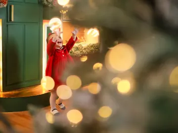 Bebê de braços abertos para cima maravilhada com as luzes quentes e o brilho do Natal no Estúdio Evydência