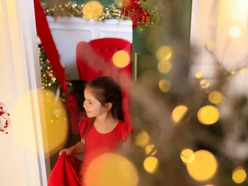 Menina de vestido vermelho espiando pelo portal verde entre luzes douradas e a poltrona aconchegante