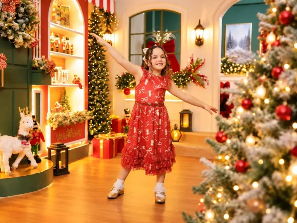 Menina rodopiando como bailarina com vestido vermelho e sapatinhos dourados no piso da Vila de Natal