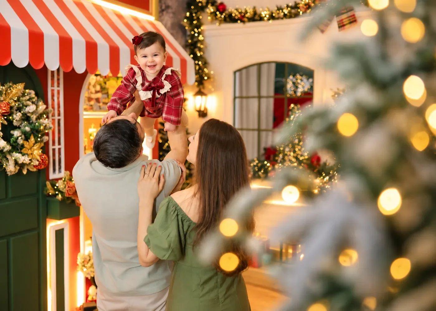 Pai erguendo a bebê no ar com a mãe sorrindo em ensaio de Natal acolhedor no Estúdio Evydência em Tijucas
