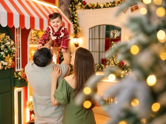 Pai erguendo a bebê no ar com a mãe sorrindo em ensaio de Natal acolhedor no Estúdio Evydência em Tijucas